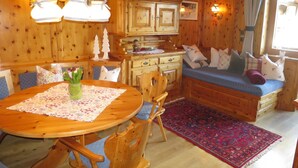 Interior de una cabaña de madera con una mesa de comedor, sillas, un banco y una zona de cocina.