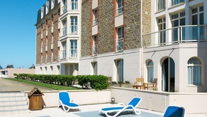A hotel with a stone facade, multiple balconies, and outdoor seating areas with lounge chairs. - Reine Marine- T2 SUD by Interhome (Saint Malo)