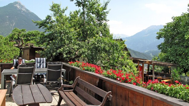 An outdoor patio with wooden furniture, a Coca-Cola sign, and a view of mountains. - Apartment Anich by Interhome (Imst)