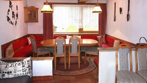 A dining area with a wooden table and chairs, a red cushioned bench, and two hanging lamps. - Apartment Anich by Interhome (Imst)