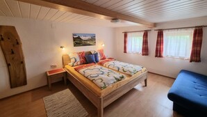 A bedroom with a wooden bed, a blue sofa, a wooden headboard, a painting on the wall, and a window with curtains.