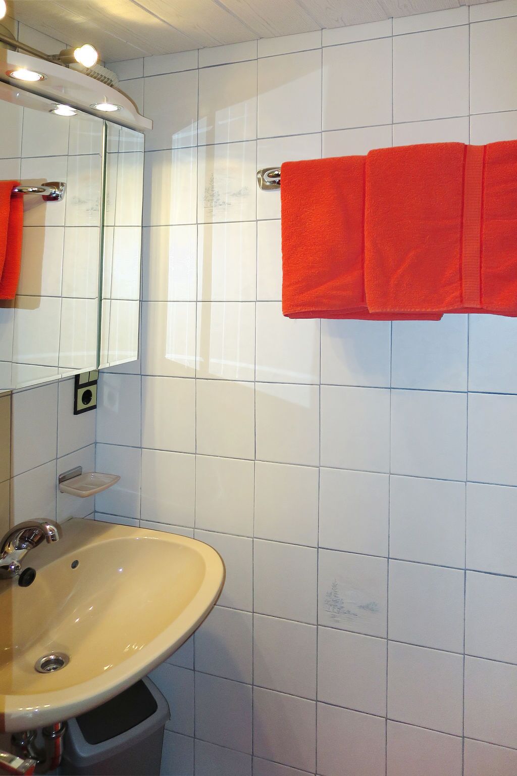 A bathroom with white tiles, a beige sink, a mirror, and a red towel on a rack.