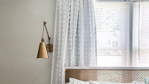 Une chambre à coucher avec un lit, une petite table ronde, une lampe et une fenêtre avec des stores.