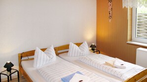 A double bed with wooden headboard and white linens, two bedside tables with lamps, and a window with a view of greenery.