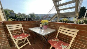 A small outdoor patio with two white chairs with floral cushions, a table with a bottle and flowers, and a brick wall.