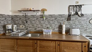 Een keuken met een betegelde spatwand, houten kastjes, een inbouwoven en diverse keukenapparaten.