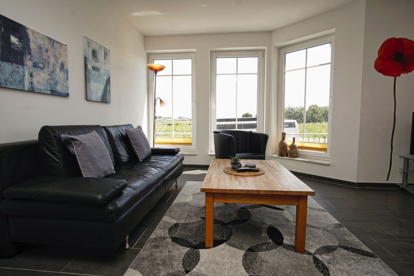 Un salón con un sofá de cuero negro, una mesa de centro de madera y ventanas amplias con vistas.