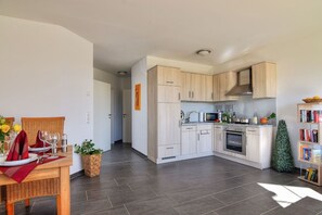 Une cuisine moderne avec des meubles de couleur bois clair, un four à micro-ondes, un four traditionnel et un petit coin repas avec une table mise pour deux personnes.