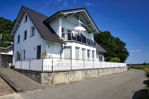 Ein zweistöckiges Haus mit Balkon, weißem Zaun und gepflasterter Auffahrt.