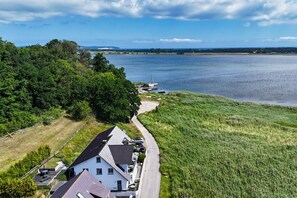 A coastal property with a road leading to a dock, surrounded by greenery and a large body of water.