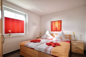 A bedroom with a wooden bed, red and white bedding, a bedside table with a lamp, and a window with red blinds. - Chic vacation apartment with sea view - rügenreif Holiday apartment no. 02 - rügenreif (Mönchgut)