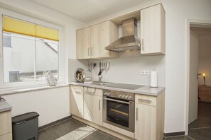 Eine moderne Küche mit hellen Holzschränken, einer Edelstahl-Dunstabzugshaube, einem eingebauten Backofen und einem Fenster mit gelben Jalousien.