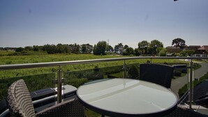 A balcony with a glass table and wicker chairs, overlooking a green landscape and buildings. - Chic vacation apartment with sea view - rügenreif Holiday apartment no. 02 - rügenreif (Mönchgut)