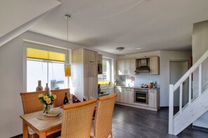 Cuina moderna amb armaris de fusta, zona de menjador amb cadires de vimetla i una escala.