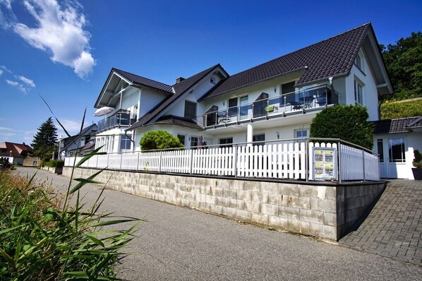 A two-story house with a white exterior, a balcony on the upper floor, and a white picket fence.