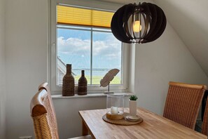 A dining area with a table, chairs, a window with a view, and a hanging light fixture.