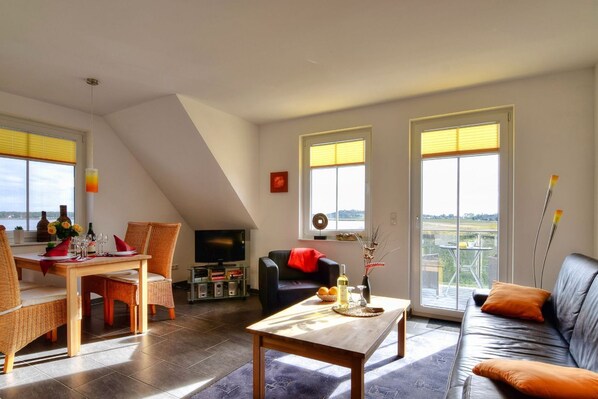 Ein Wohnzimmer mit Essbereich, einer schwarzen Ledersofa, einem Holztisch und einem Fernseher.