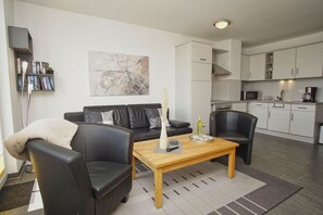 A modern living room with a sofa, chairs, a coffee table, and a kitchen area in the background.