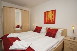 Una habitación de hotel con cama, armario, mesita de noche, lámpara y un cuadro en la pared.