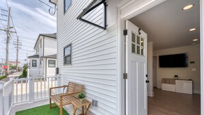 A residential entryway with a wooden bench and a small potted plant, a white door, and a flat-screen TV in the adjacent room. - GAME ROOM-Downtown Remodeled Single Family House (Ocean City)