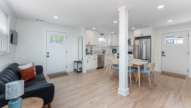 A modern kitchen with white cabinets, a dining area with wooden chairs, and a black sofa with a lamp. - GAME ROOM-Downtown Remodeled Single Family House (Ocean City)