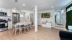 A modern kitchen with white cabinets, stainless steel appliances, and a dining area with wooden chairs and a table. - GAME ROOM-Downtown Remodeled Single Family House (Ocean City)