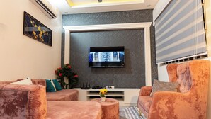 A modern living room with a flat-screen TV mounted on the wall, a sofa set, a coffee table, and a decorative plant.