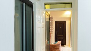 A hallway with a glass door leading to a room, a brown cushioned bench, and a door at the end.