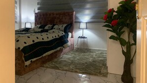 Een slaapkamer met een bed, nachtkastje, lamp, kamerplant en een raam met zonwering.