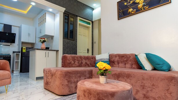 Een moderne woonkamer met een zithoek, een salontafel met bloemen, en een keuken op de achtergrond.