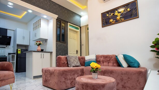 A modern living room with a pink sectional sofa, a round ottoman, and a small table with a vase of flowers.