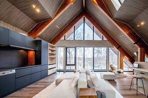 A modern loft with a high ceiling, exposed wooden beams, a large window, and a cozy seating area. - Vader (Kutchan)