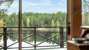 Una terraza de madera con barandilla de metal que da a un lago, rodeada de un bosque frondoso.
