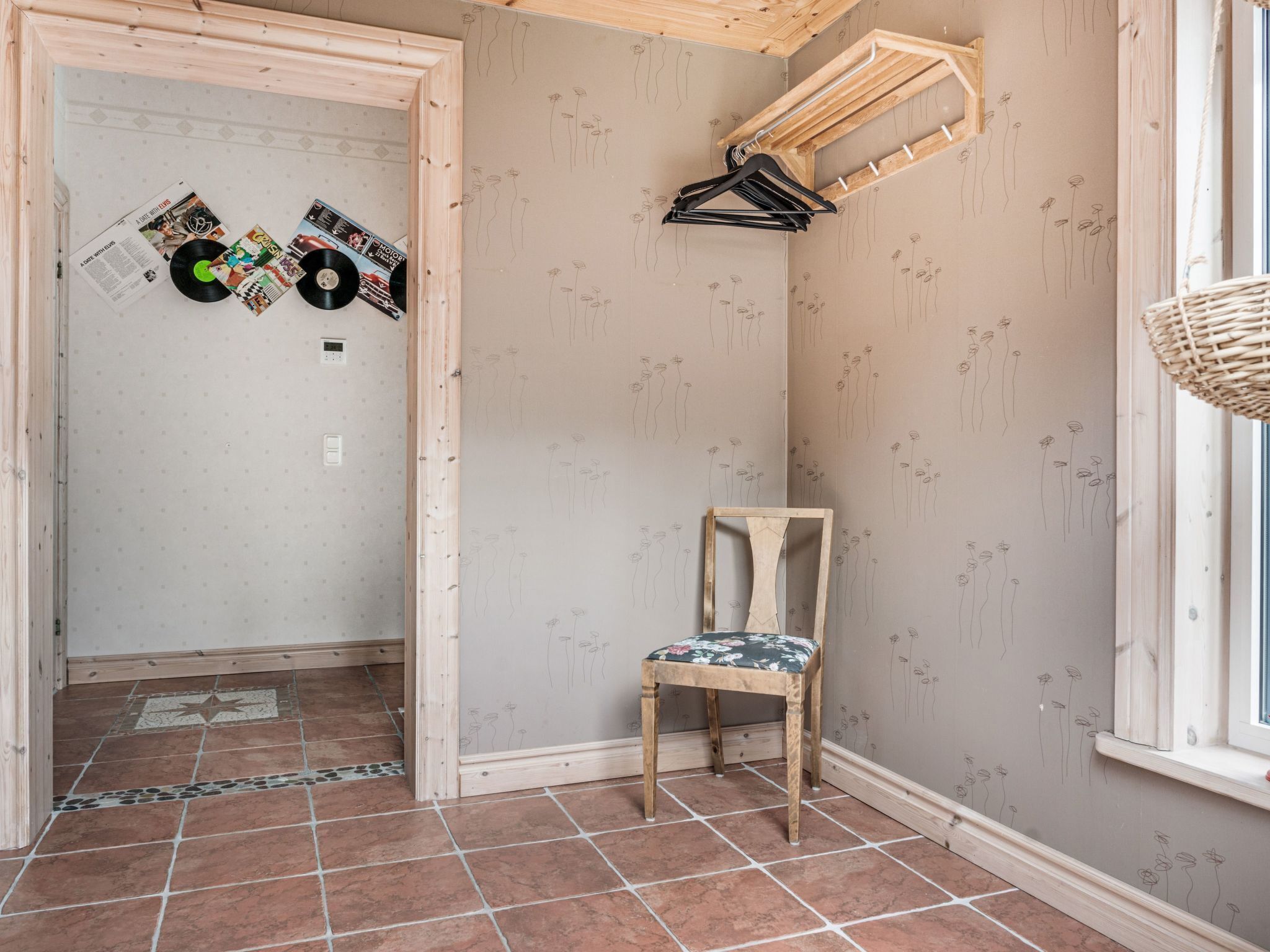 A room with a wooden chair, a wall-mounted coat rack, and a door with a tiled floor.