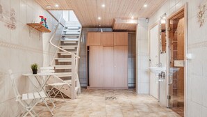Un pasillo con una escalera de madera, una pequeña mesa con una planta y un piso de baldosas con un diseño decorativo.