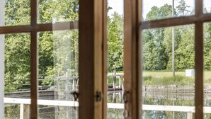 A view through a window with a wooden frame, reflecting a pond, a wooden dock, and a grassy area with trees. - Tingsmåla by Interhome (Tingsryd)