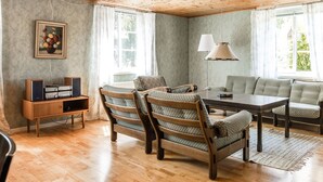 A cozy room with wooden flooring, a dining table with chairs, a sofa, a lamp, and a speaker system. - Gåragöl by Interhome (Olofström)