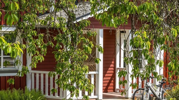 A red building with a white porch, a bike parked outside, and a stone structure in the foreground. - Gåragöl by Interhome (Olofström)