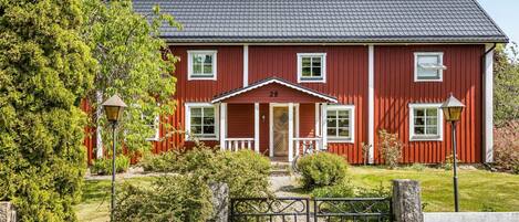A red two-story house with a white porch, a chimney, and a small garden with a gate.