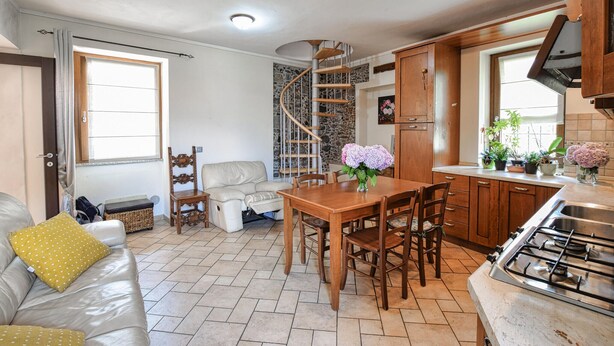 A compact kitchen with a dining area, a spiral staircase, and a sofa with cushions.