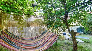 A hammock hanging between bamboo poles, a tree, and a white fence in a garden.