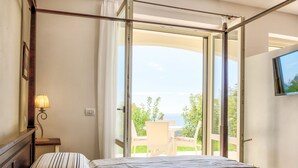 A hotel room with two beds, a window with a view of greenery and a building, a lamp, and a TV mounted on the wall. - Villa di Sogno by Interhome (Lacona)