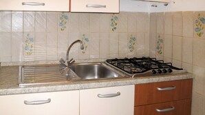 A kitchen with a stainless steel sink, a gas stove, and white cabinets with silver handles.