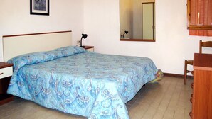 A bedroom with a bed, a nightstand, a desk, a chair, a mirror, and a framed picture on the wall.