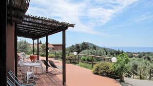 Une terrasse extérieure avec des tables et des chaises, une pergola et une vue sur la mer et les collines.