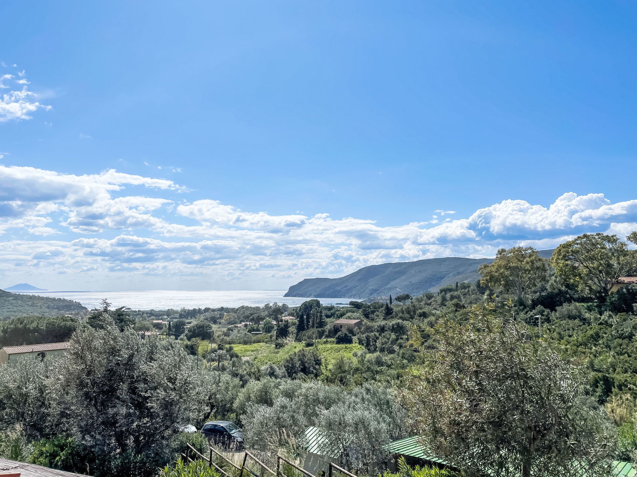 A coastal landscape with a view of the sea, hills, and scattered buildings.
