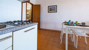 Une cuisine équipée d’une cuisinière à gaz, de meubles blancs et d’un coin repas avec des chaises et une table, le tout dans des tons blancs.