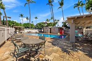 A pool area with lounge chairs, a table, and a small building with a sign. - Legal STR w/ Sunset & Ocean Views, Penthouse Unit (Kihei)