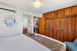 Une chambre d’hôtel avec un lit, une armoire en bois, un miroir décoratif et un coin repas visible à travers une porte ouverte.