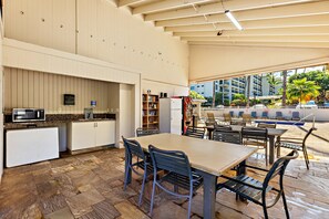 A spacious indoor area with a kitchen, dining table, and chairs, leading to an outdoor seating area with a pool view.